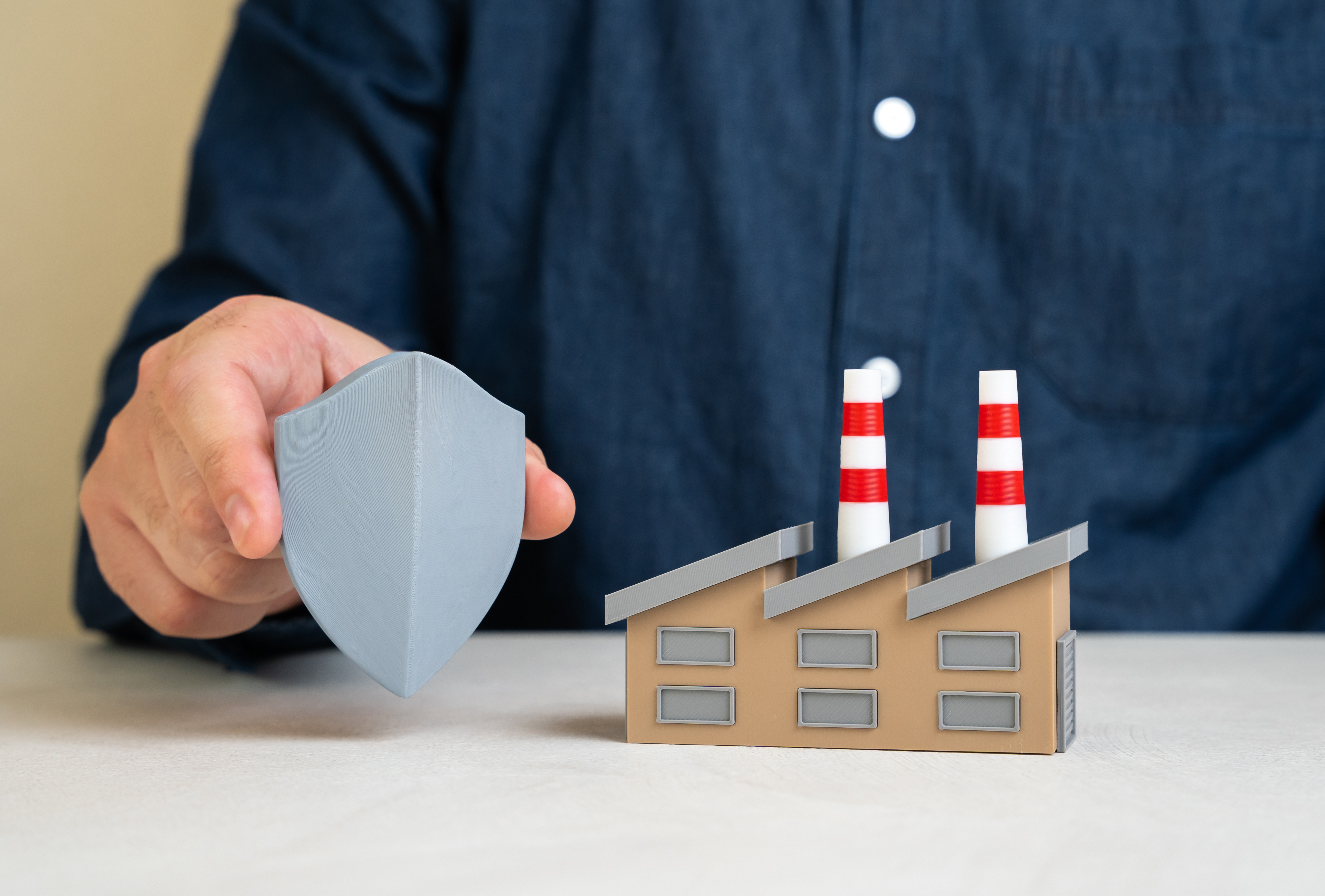 A model of a factory with smokestacks, with someone holding a small shield next to it.