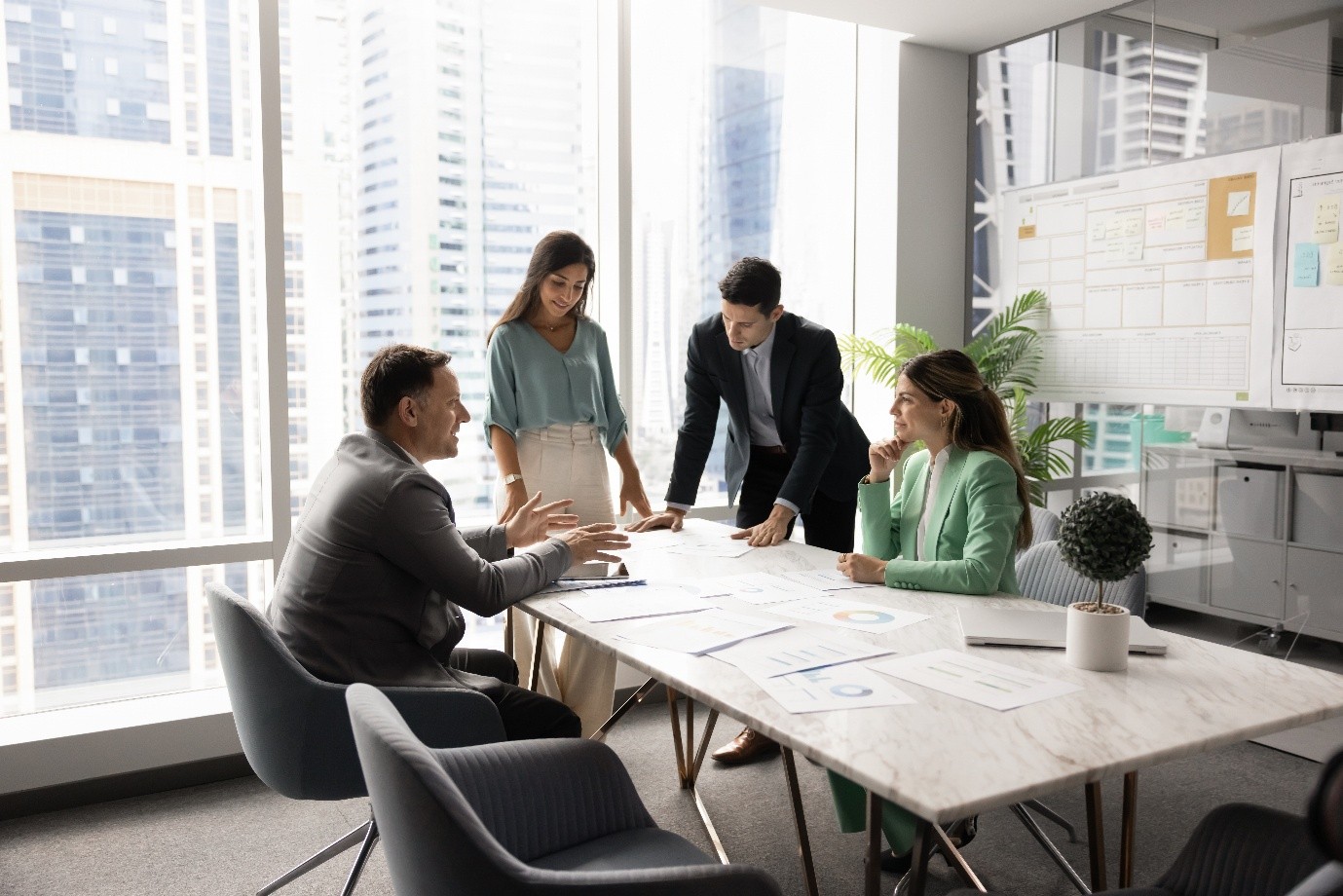 Four people around a board table in an office discussing the papers spread across it.